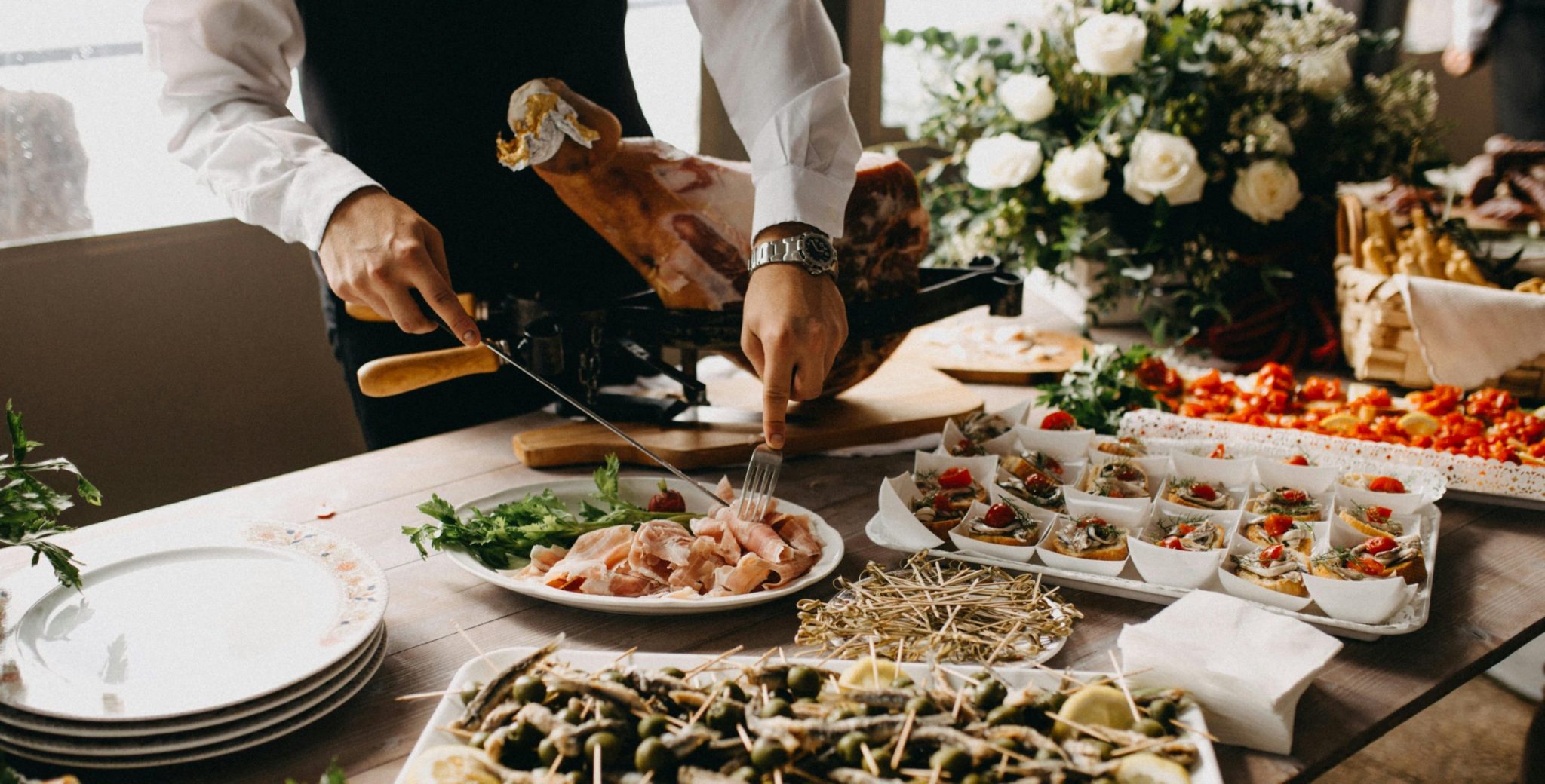 A chef slices meat in a beautifully arranged catering setup with diverse appetizing dishes.